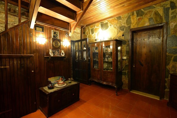 Una habitación con paneles de madera, una pared de piedra, un mueble de madera con puertas de cristal y suelo de baldosas.