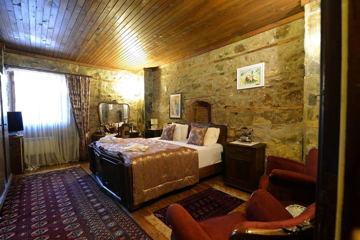 A traditional room with a bed, a wooden ceiling, stone walls, and a red carpet.