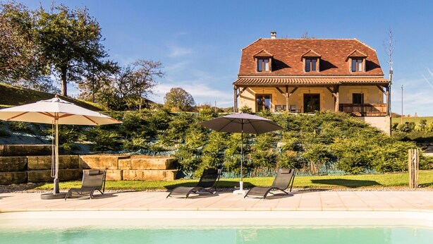 Una casa con piscina, rodeada de un jardín y dos sombrillas.