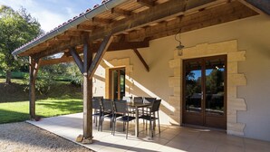 Un patio cubierto con mesa y sillas, paredes de piedra y vistas del paisaje circundante.