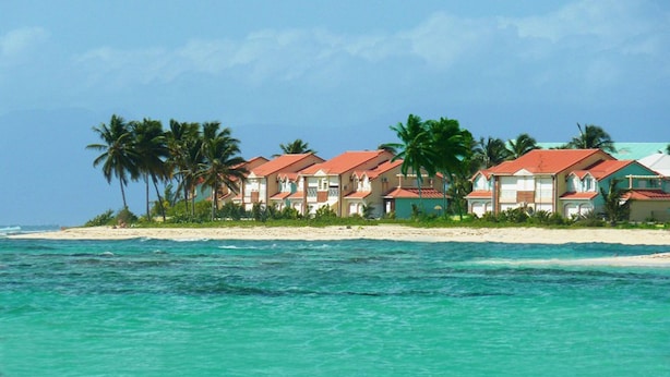 Ein Hotel direkt am Strand, bestehend aus mehreren Gebäuden, mit Palmen und einem Sandstrand.
