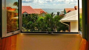 Ein Zimmer mit großem Fenster und Blick auf eine Küstenlandschaft mit Häusern und Palmen.