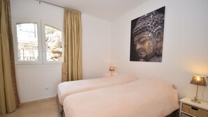 Un dormitorio con dos camas, una ventana con cortinas, una estatua de Buda en la pared y una lámpara de noche.