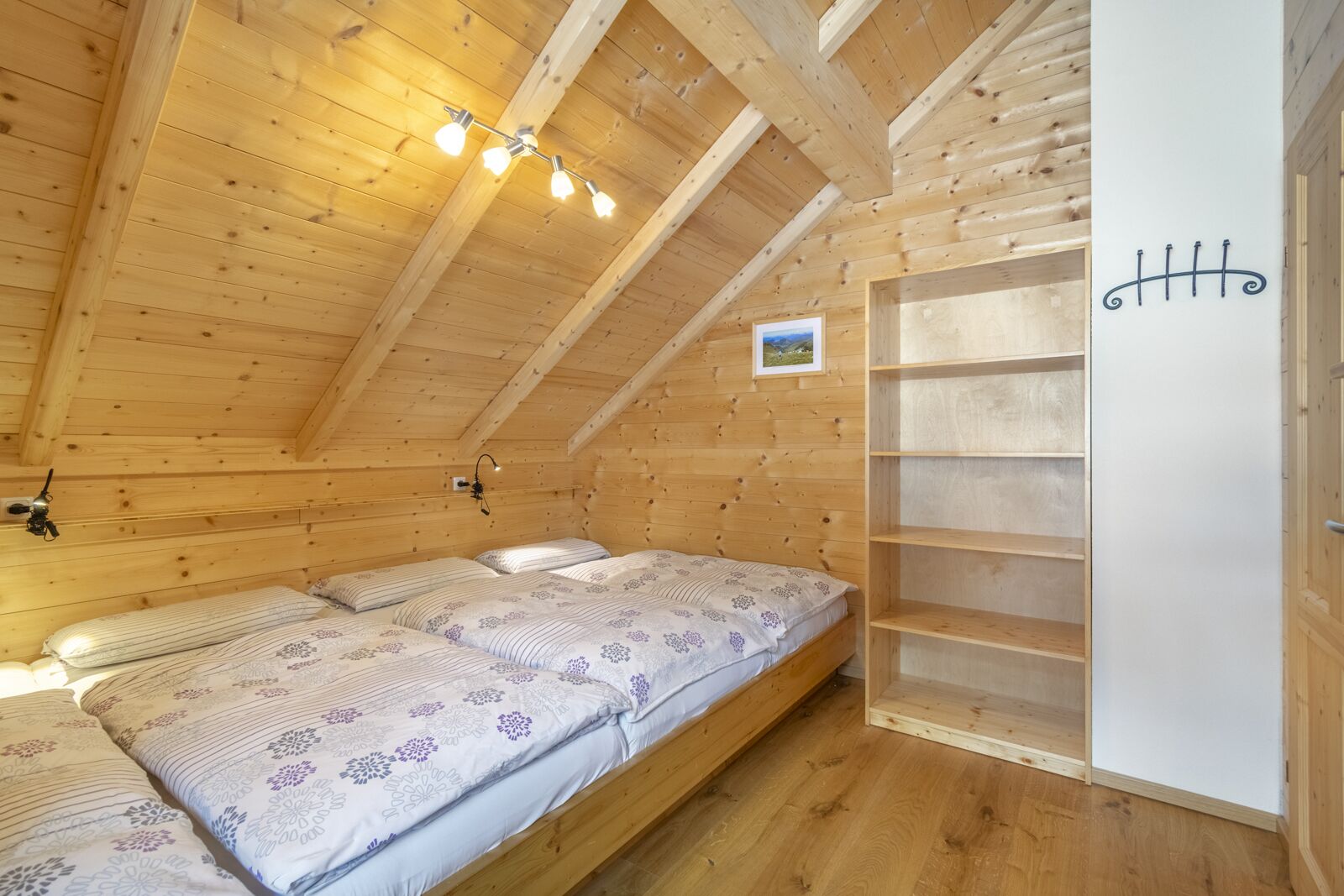 Ein Zimmer einer Holzjagdhuette mit einem Schlafkoje und einem kleinen Regal sowie einem Bild an der Wand.