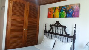 A bedroom with a wooden wardrobe, a bed with white bedding, and a colorful painting of parrots on the wall. - HOUSE COAST, on Faial Island, Azores (HORTA)