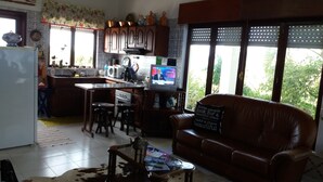 A kitchen with a dining area, a sofa, and a TV displaying a news channel. - HOUSE COAST, on Faial Island, Azores (HORTA)