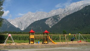 A playground with climbing structures and slides, set against a backdrop of mountains and a clear sky.