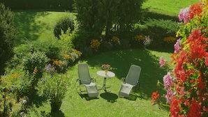 A well-maintained garden with a small table and two chairs, surrounded by various plants and flowers.