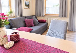 A modern living room with a grey sofa, red and grey cushions, a white vase with flowers, a patterned rug, and a grey armchair. - Adlerhof am Sonnenplateau Vacation Rental in Mieming, Pet-Free and Allergy-Friendly (Wildermieming)