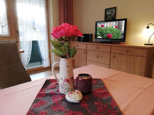 Quarto com armário de madeira, televisão, um vaso com flores e mesa com jogo americano.