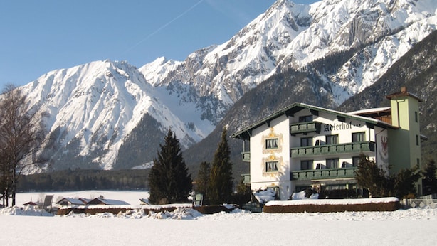 A hotel with a traditional Alpine architectural style, surrounded by snow-covered mountains and a clear sky.