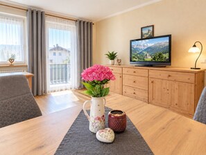 A modern living room with a wooden dining table, a television, and a potted plant.