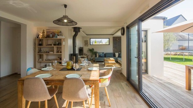 A modern living room with a wooden dining table, chairs, and a sofa. There is a bookshelf, a fireplace, and a large window. - Luxury house with heated Jacuzzi 3km from the center of Vannes  (Ploeren)