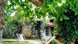 Un jardí amb dues cadires de fusta, una paret de pedra i una casa amb una porta verda i finestres.