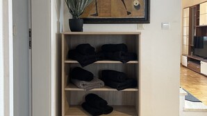 A hallway with a wooden shelf holding black towels, a potted plant, and a framed artwork above.