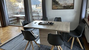 A modern dining area with a wooden table, black chairs, and a city view through large windows.