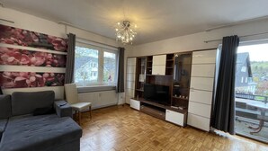 A modern living room with a sofa, TV, wooden floor, and a large window with curtains.