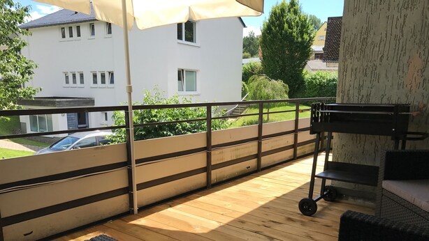 A wooden deck with outdoor furniture, a metal railing, and a view of a white building in the background.