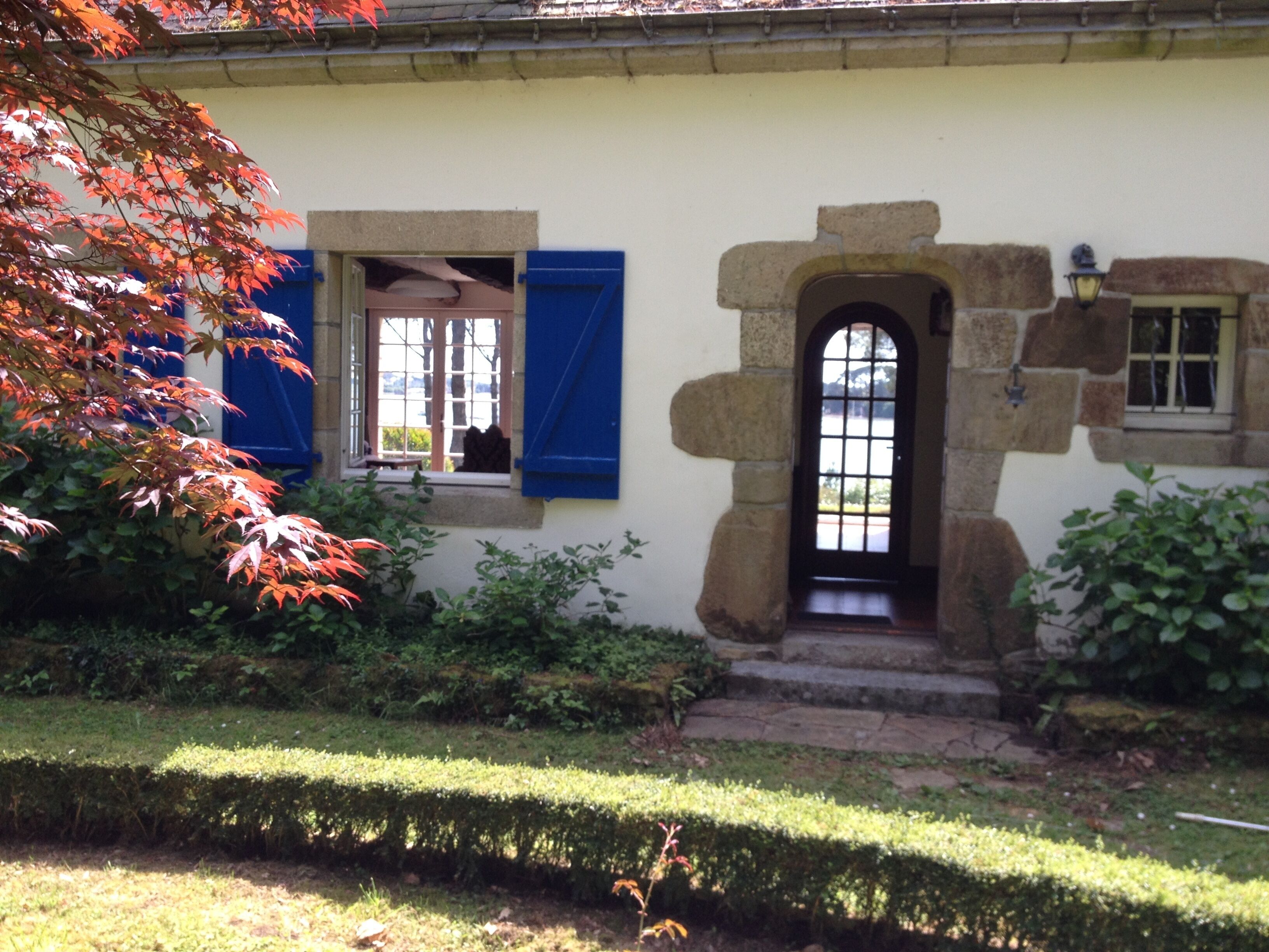 A house with a stone entrance, a small window with blue shutters, and a door with a glass panel.