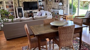 Un salon chaleureux avec un mur en pierre, une cheminée, un téléviseur et un coin repas agrémenté de meubles en osier.