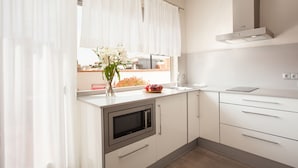 A modern kitchen with white cabinets, a built-in microwave, and a window with sheer curtains. - Studio apartment Barcelona with terrace (Barcelone)