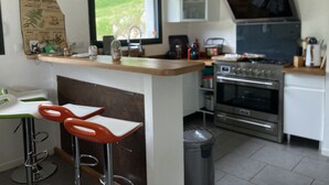 A modern kitchen with a central island, bar stools, a stove, oven, and a window overlooking a garden. - Modern and comfortable chalet with stunning views of the Ariege Pyrenees (Gestiès)