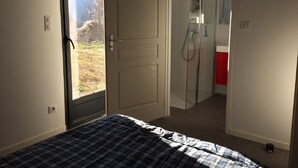 A bedroom with a bed, a door leading to a bathroom, and a view of the outdoors. - Modern and comfortable chalet with stunning views of the Ariege Pyrenees (Gestiès)