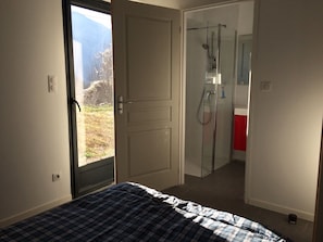 Ein Schlafzimmer mit einem Bett, einer Tür zum Badezimmer und Blick ins Freie.
