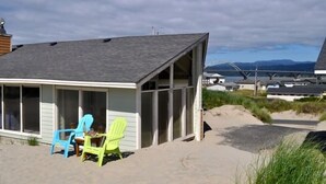 Et strandhus med en overdækket veranda, to stole og udsigt til stranden og bjergene.