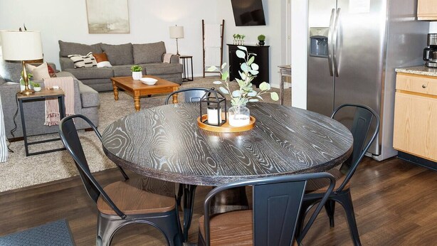 A modern living room with a grey sofa, a coffee table, and a dining table with chairs. There is a kitchen area with a refrigerator and a stove. - Team or Family Stay/Peloton/1.9 mile to Grand Park (Westfield)