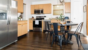 A modern kitchen with wooden cabinets, stainless steel appliances, and a dining area with black chairs. - Team or Family Stay/Peloton/1.9 mile to Grand Park (Westfield)