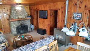 A cozy cabin interior with a stone fireplace, a television mounted on the wall, and a wood-burning stove. - Bayview Fireside Cabin (Tower)