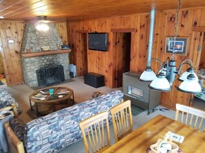 Interior acogedor de una cabaña con chimenea de piedra, televisor montado en la pared y estufa de leña.