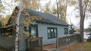 Eine Holzhütte mit einer Holzdiele, umgeben von Bäumen mit Herbstlaub.