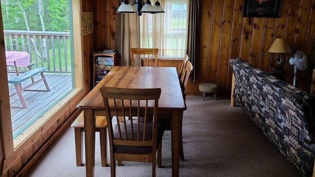 A wooden cabin interior with a dining table, chairs, a sofa, a television, and a window overlooking greenery. - Bayview Fireside Cabin (Tower)