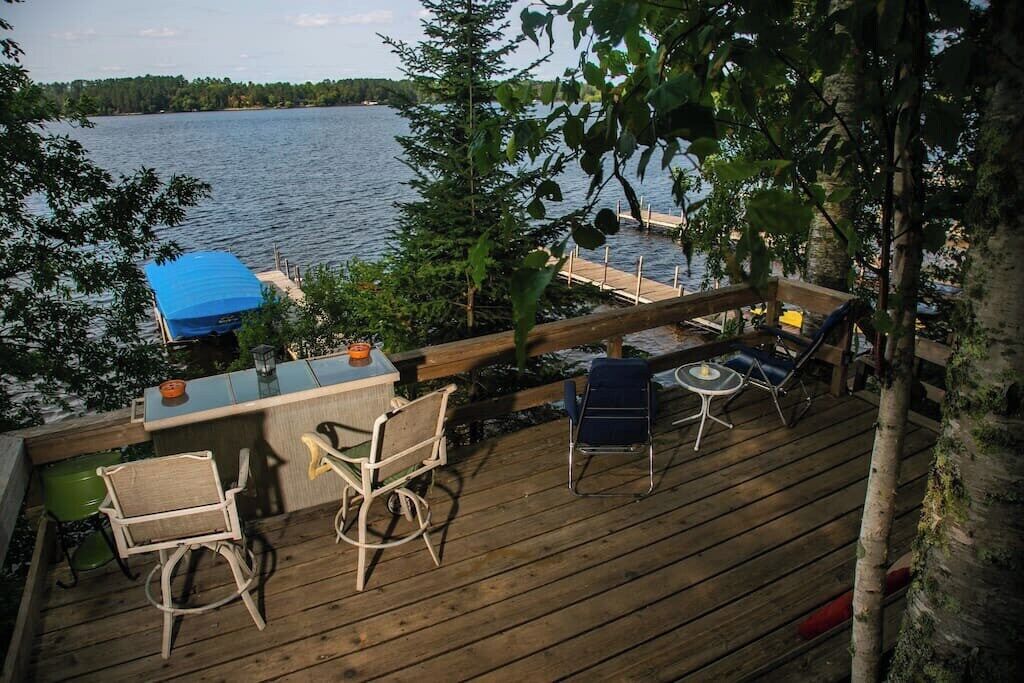A wooden deck with outdoor furniture, a bar area, and a view of a lake.