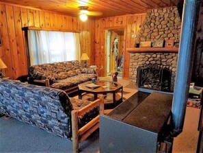 L’intérieur d’un chalet chaleureux, avec un ensemble de canapés, une cheminée et un mur en pierre.