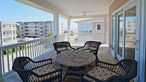 A covered outdoor deck with wicker furniture and a round table, overlooking a residential area and the ocean. - The Ultimate In Beach Living! Ocean View, Steps to Beach,  Sleeps 8. Elevator! (Tybee Island)