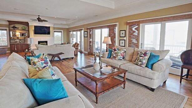 A spacious living room with a large sofa, a coffee table, and a fireplace. There is a television mounted on the wall and a ceiling fan. - The Ultimate In Beach Living! Ocean View, Steps to Beach,  Sleeps 8. Elevator! (Tybee Island)