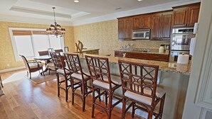 A spacious kitchen with wooden cabinets, a granite countertop, and a dining area with wooden chairs. - The Ultimate In Beach Living! Ocean View, Steps to Beach,  Sleeps 8. Elevator! (Tybee Island)