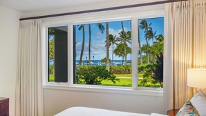 Een hotelkamer met een groot raam met uitzicht op palmbomen en de oceaan.