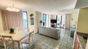 A spacious living area with a sofa, dining table, and chairs, a television, and a view of the sea through large windows. - AUGUST REDUCED/SEPTEMBER AVAILABLE!! (Orange Beach)
