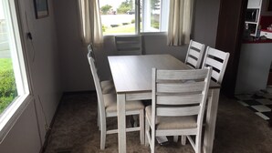 A dining area with a wooden table and four chairs, carpeted floor, and a window with curtains.