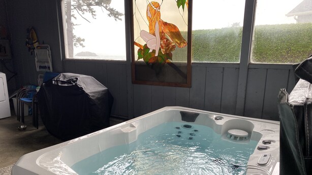 A hot tub with a view of the outdoors, a chair, and a covered table.