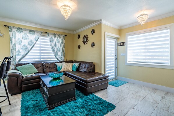 A living room with a brown leather sectional sofa, a dark coffee table, teal rugs, and decorative wall mirrors.