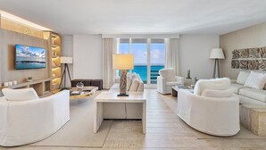 Un moderno cuarto de hotel con un gran ventanal que ofrece vistas al mar, un televisor de pantalla plana montado en la pared y una zona de estar acogedora con una mesita de centro.