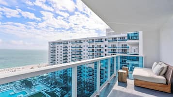 Ein moderner Hotelbalkon mit Pool, Loungebereich und Blick auf das Meer sowie andere Gebäude.
