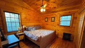 Un dormitorio de cabaña de madera con una cama, un escritorio y dos ventanas.