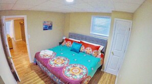 Un dormitorio con cama, una puerta, una ventana con persianas y un pasillo.
