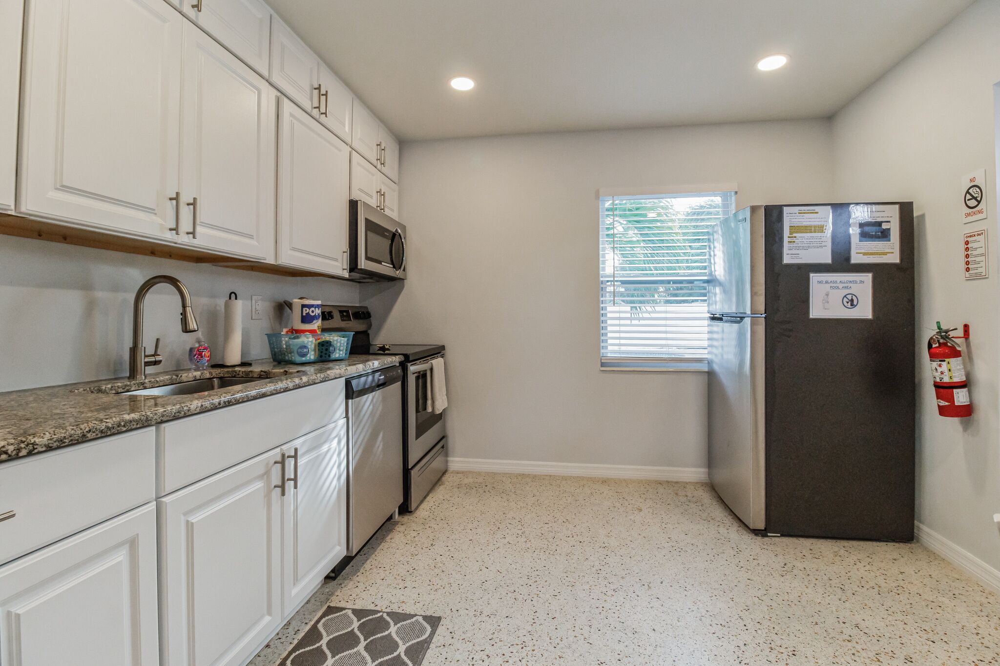 A compact kitchen with white cabinets, a stainless steel refrigerator, a microwave, and a dishwasher.